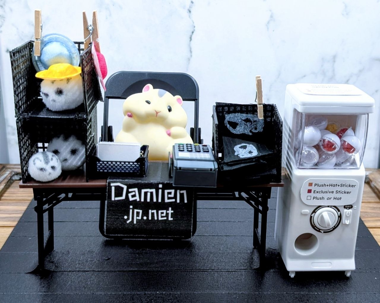 Damien the hamster (toy) sitting at a miniature artist alley booth